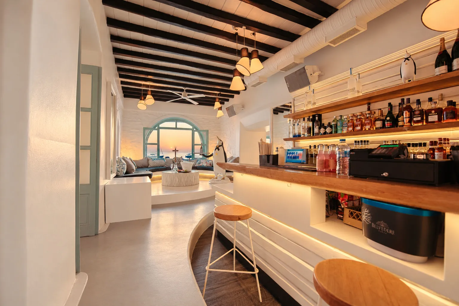 The bar counter inside BAO'S at sunset, bottles along the lit shelves and the arched window at the far end