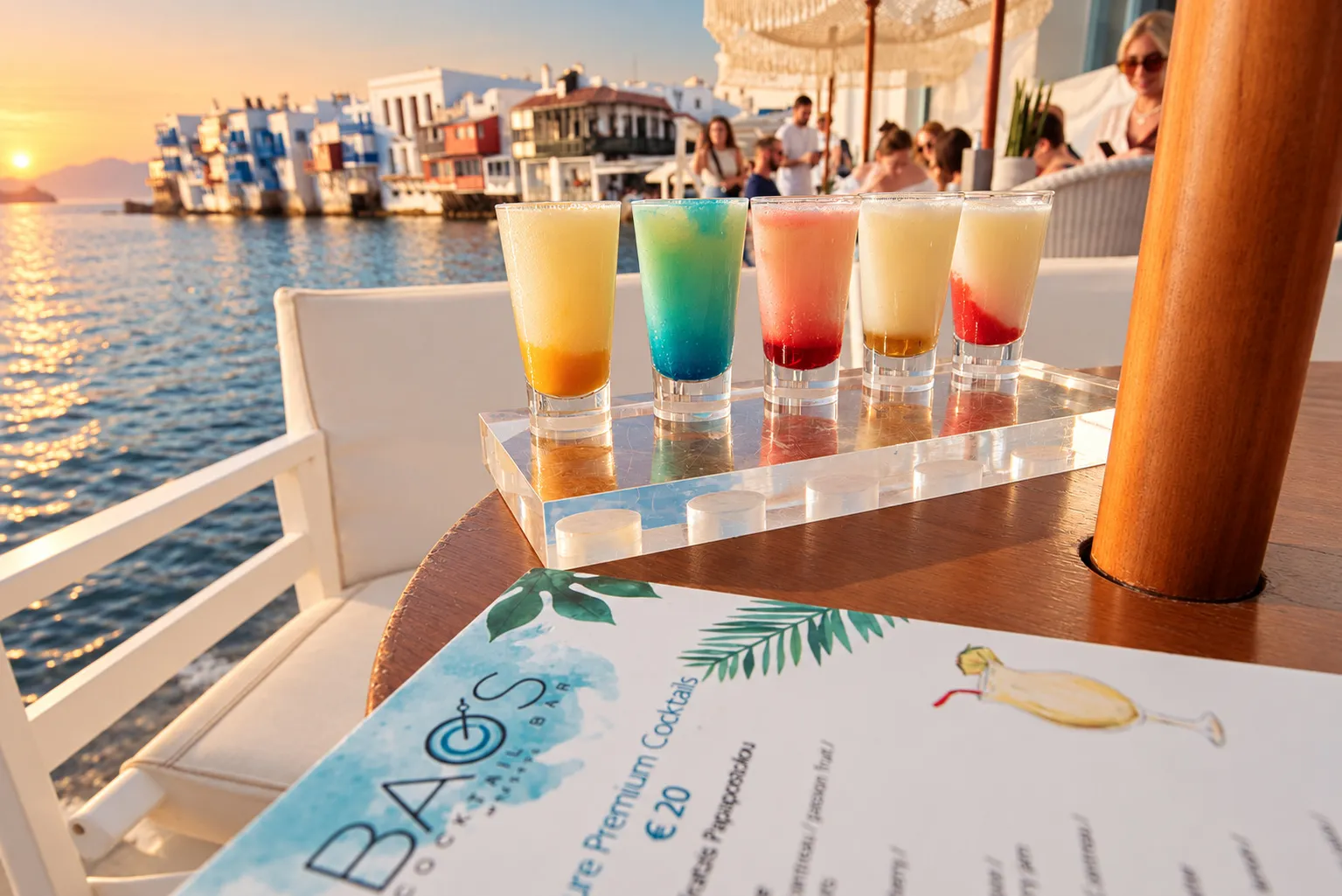 A row of five coloured cocktails on a table at BAO'S with the houses of Little Venice and the sunset behind