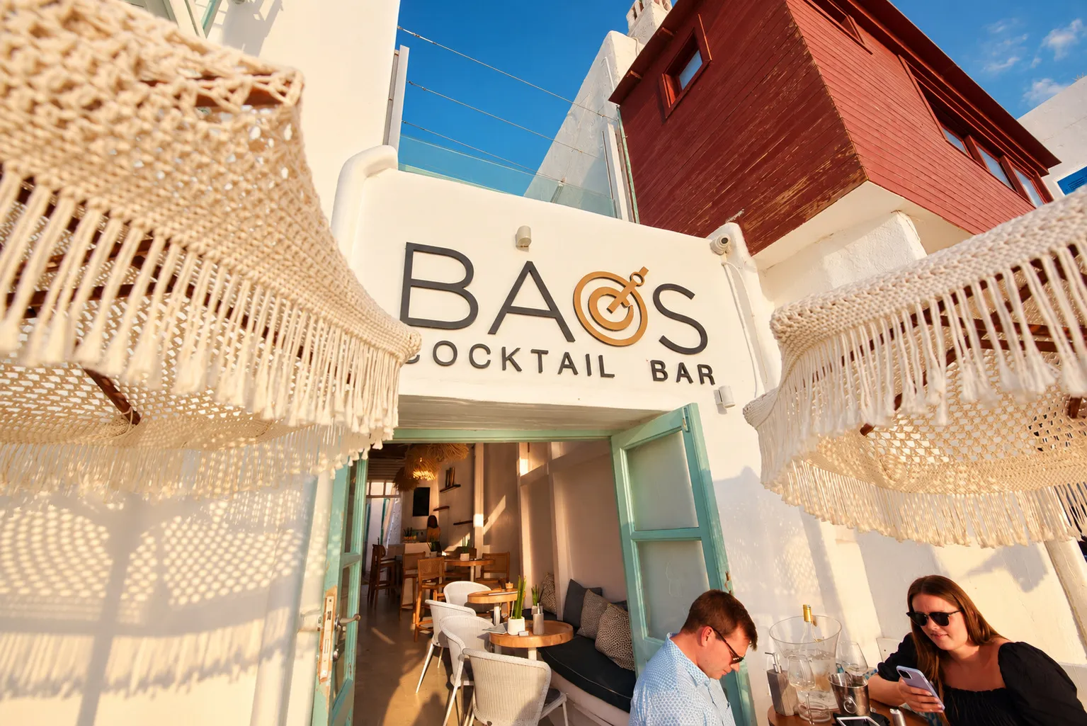 The BAO'S Cocktail Bar sign on the white wall, seen from under the macramé parasols on the waterfront