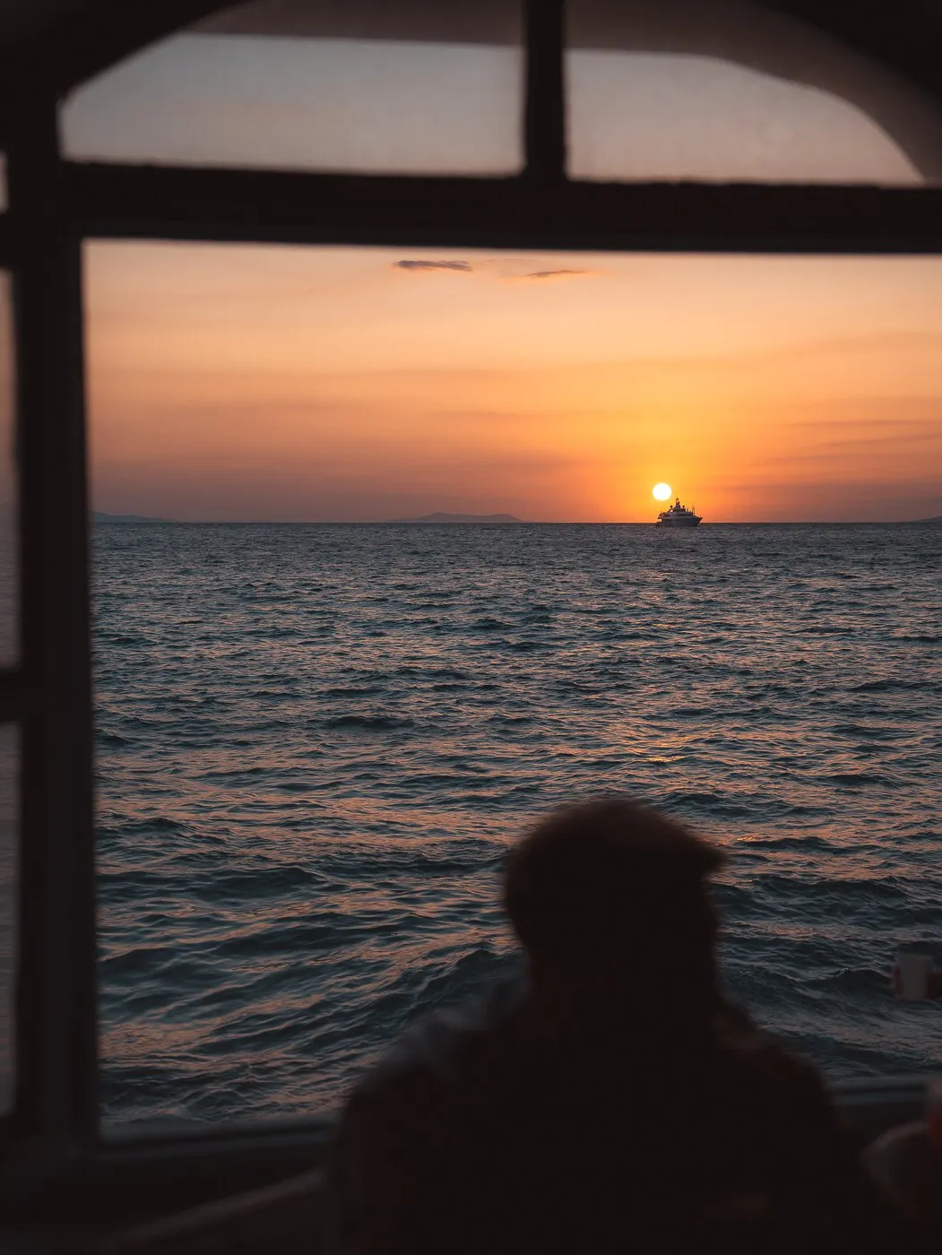 The sun going down over the sea through an arched window at BAO'S, a guest in silhouette below it