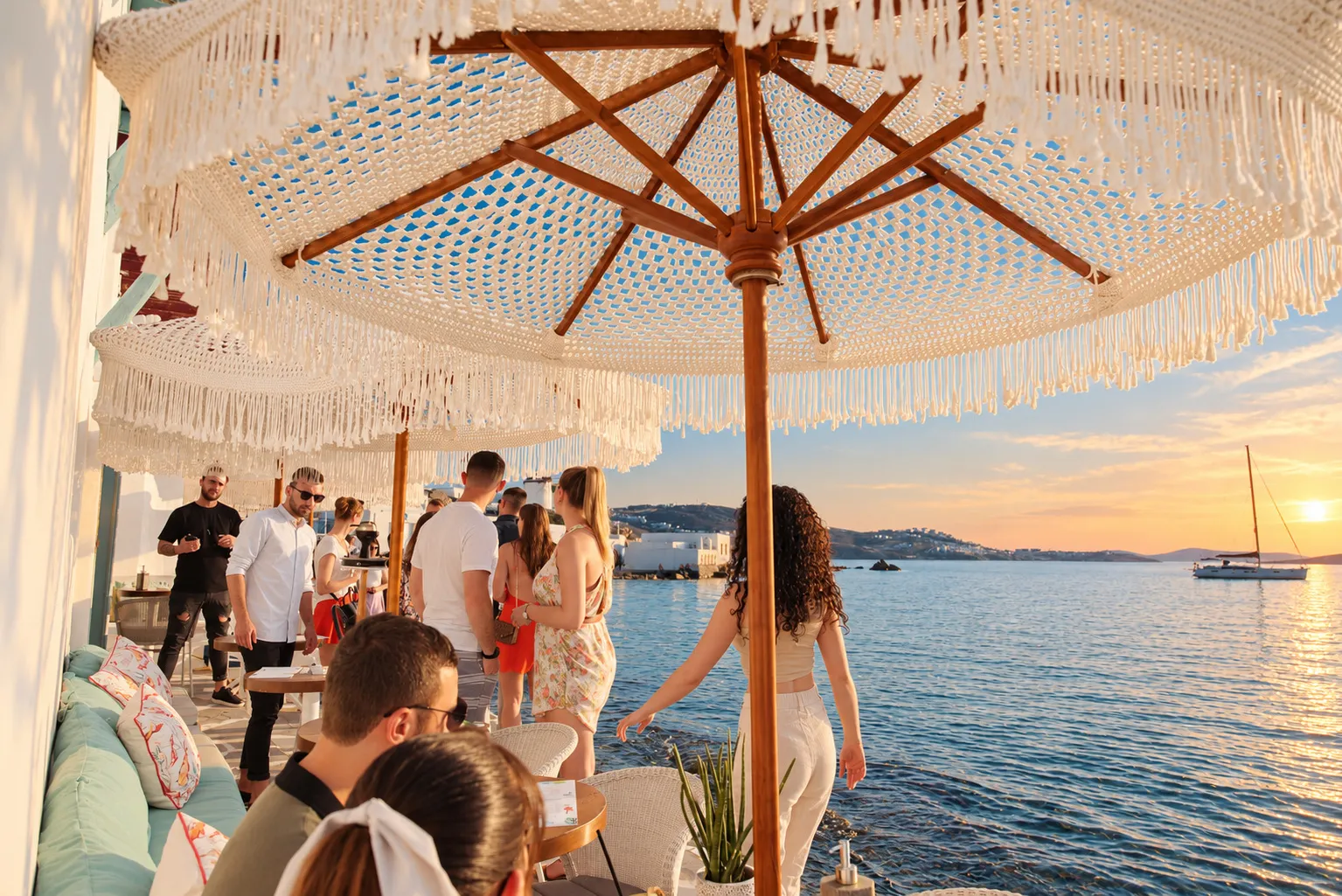 A macramé parasol over a seafront table at BAO'S, guests with cocktails and the sun going down over the sea