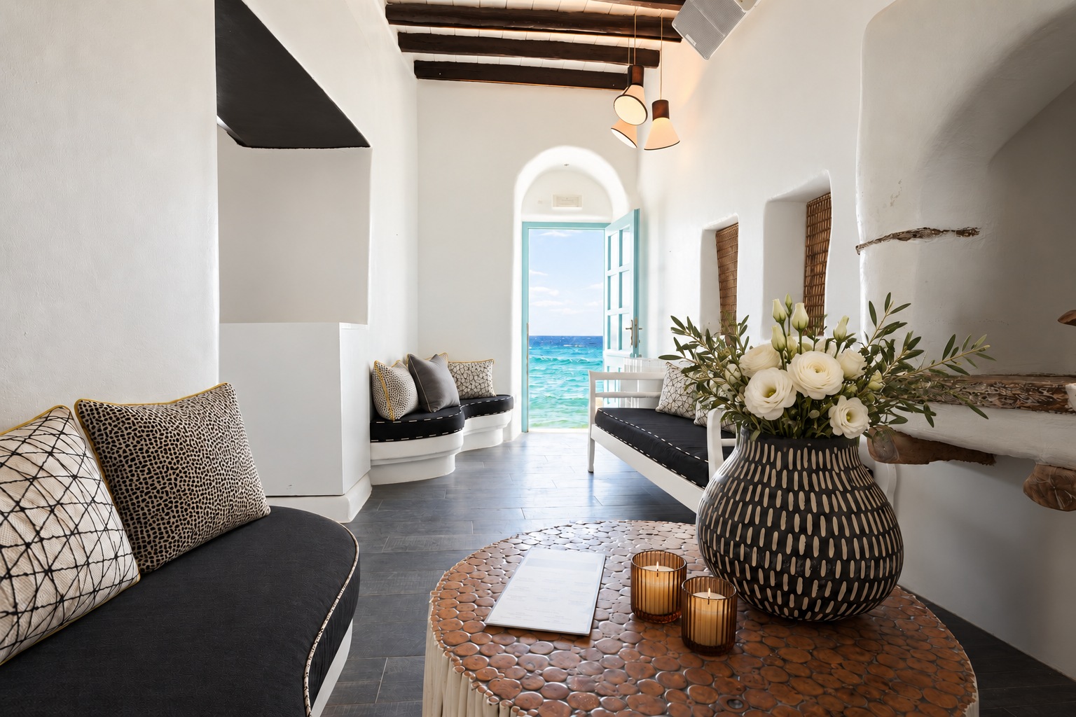 The Room in daylight, its door open onto the turquoise water of Little Venice, with the pebble-topped table and the white benches
