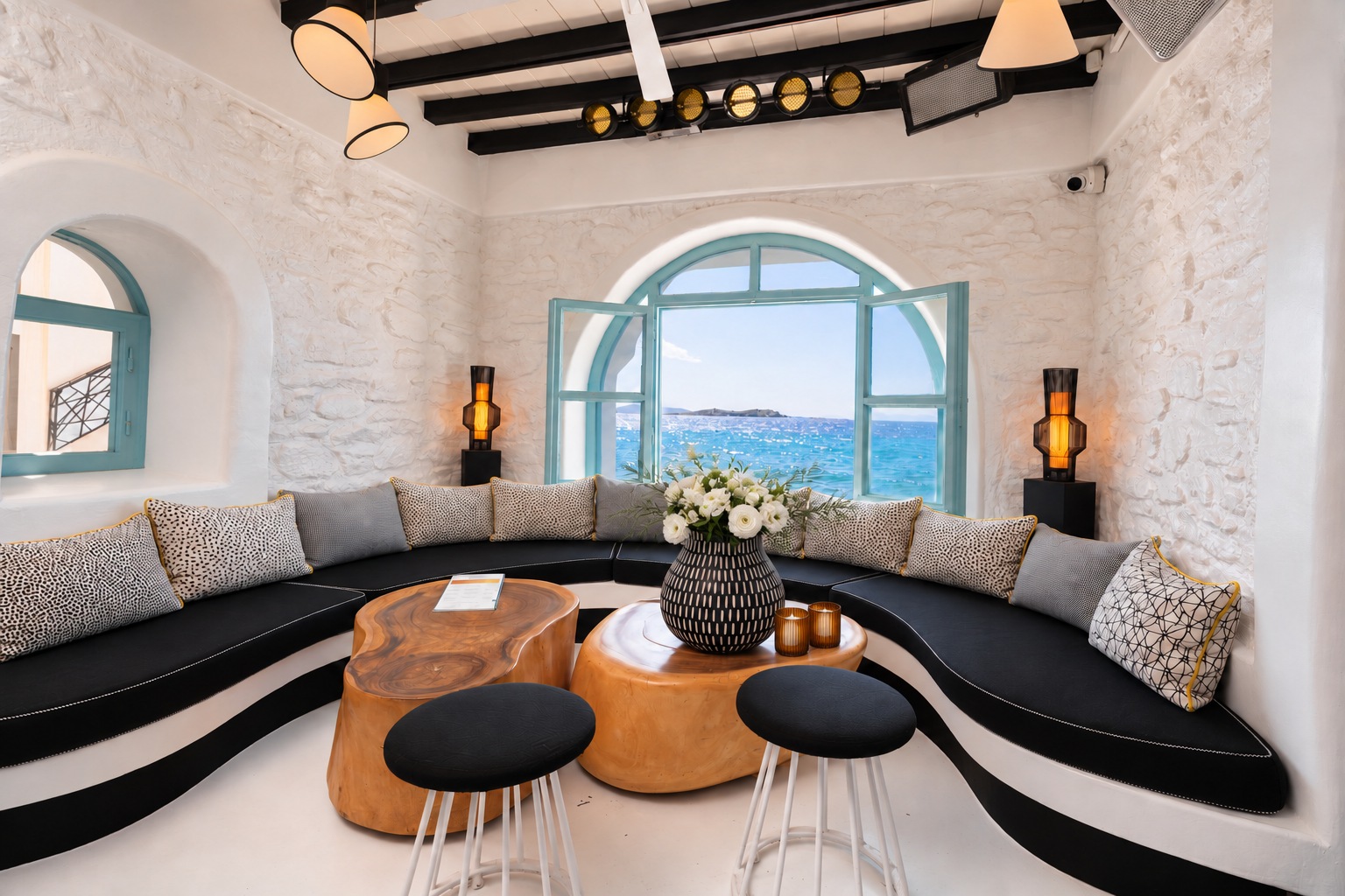 The Rotonda Table in daylight, a curved black banquette around two amber wooden tables, with the arched window open to the blue sea