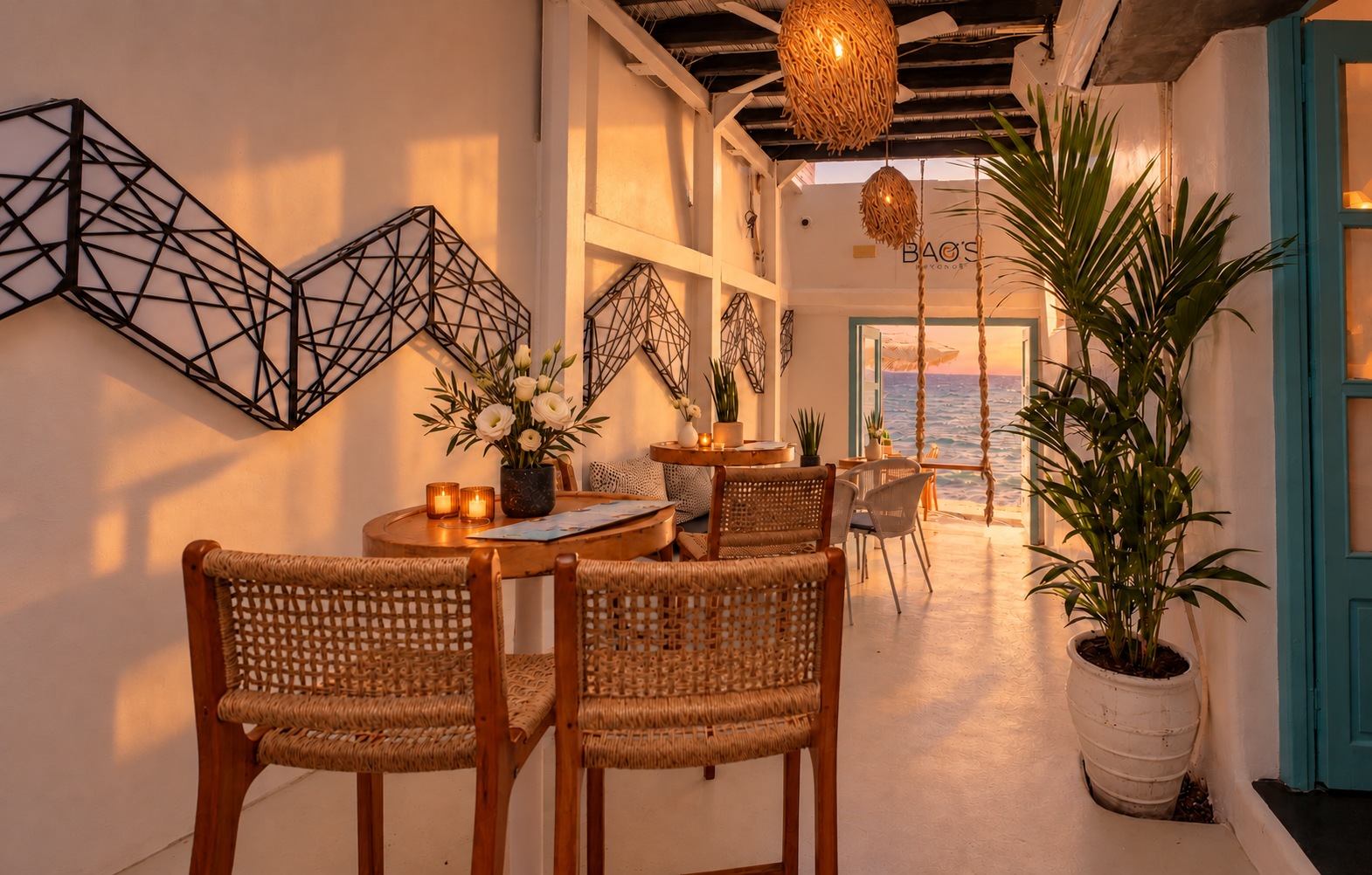 The same walkway in sunset light, the lamps lit and warm colour across the white walls, the sea still visible in the doorway